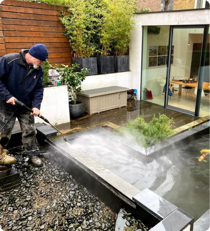 a man using a water hose to clean a pond