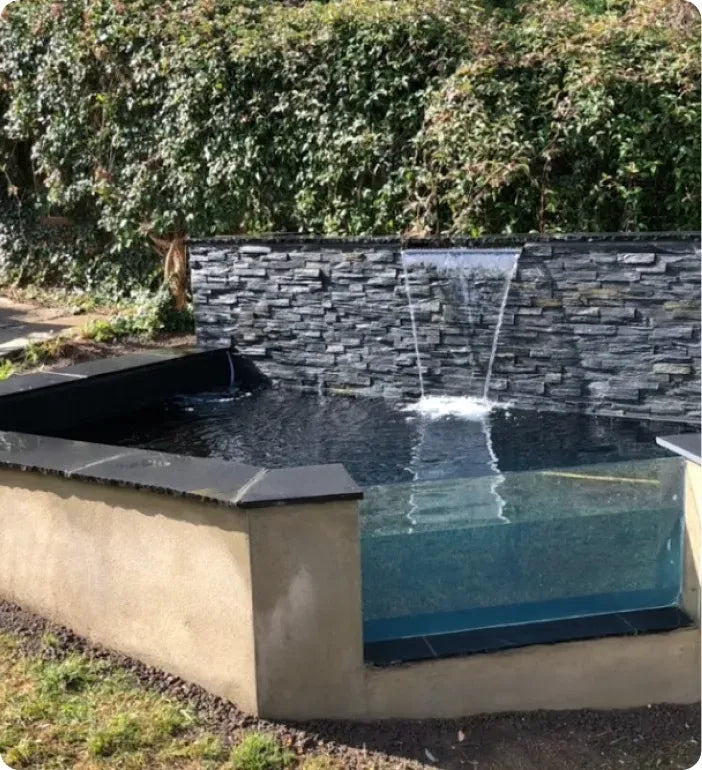 a water fountain in a garden with a stone wall behind it