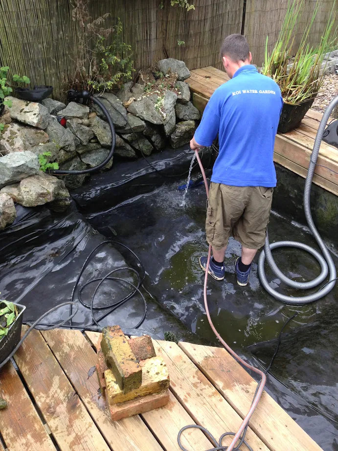 a man using a water hose to clean a pond