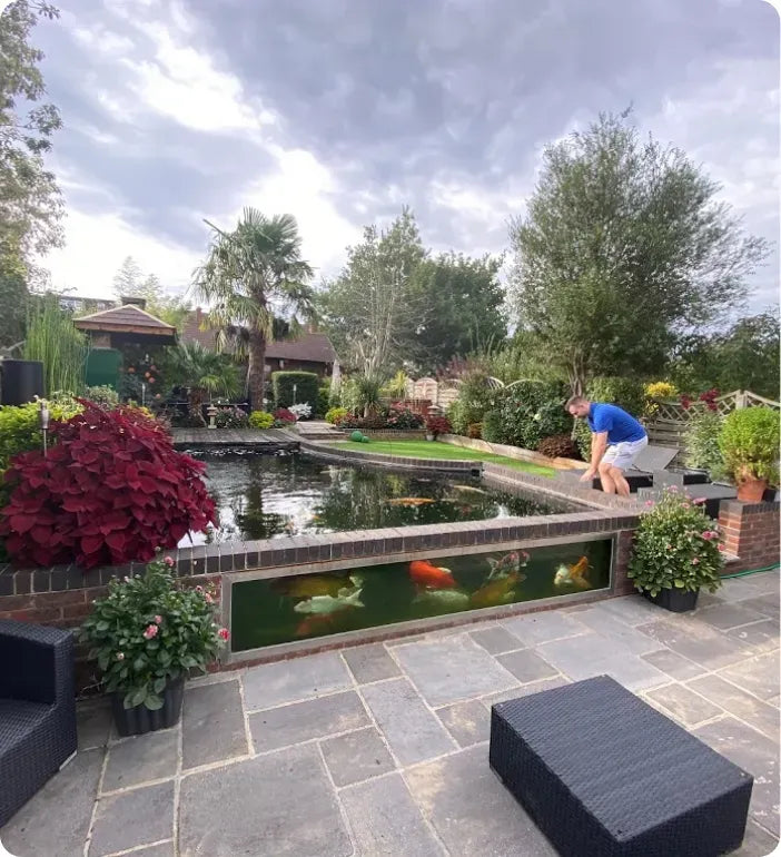 a man kneeling down to look at a fish in a pond